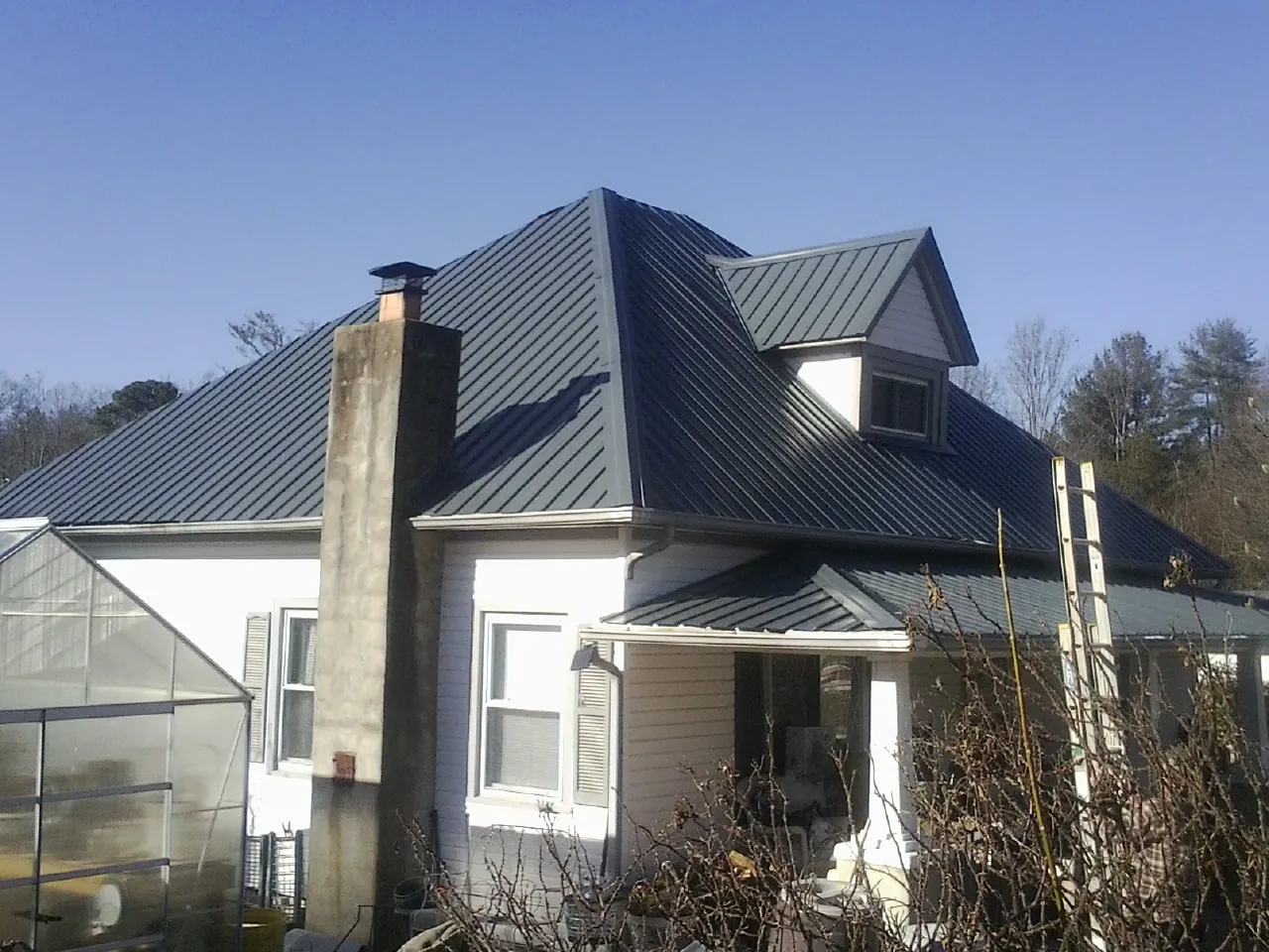 Dark blue standing seam metal roof on a white farmhouse with dormer — Slate & Tile Roof Repair by Roofing Brothers in Stitzer