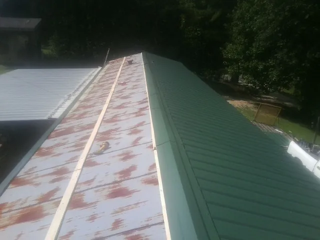 Old rusted panels beside newly installed green metal roofing — Wind Damage Roof Repair by Roofing Brothers in Stitzer