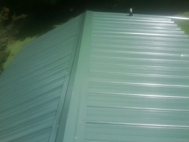New green metal panels meeting at the ridge of a roof — Flat Roof Repair work by our crew in Stitzer