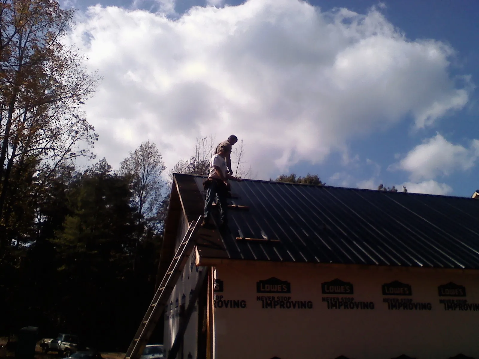 Roofer fastening dark metal panels high against a cloudy sky, from a Roof Inspection job in Stitzer